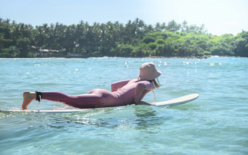 Young woman surfer in pink special swimming suit and hat going to surfing.